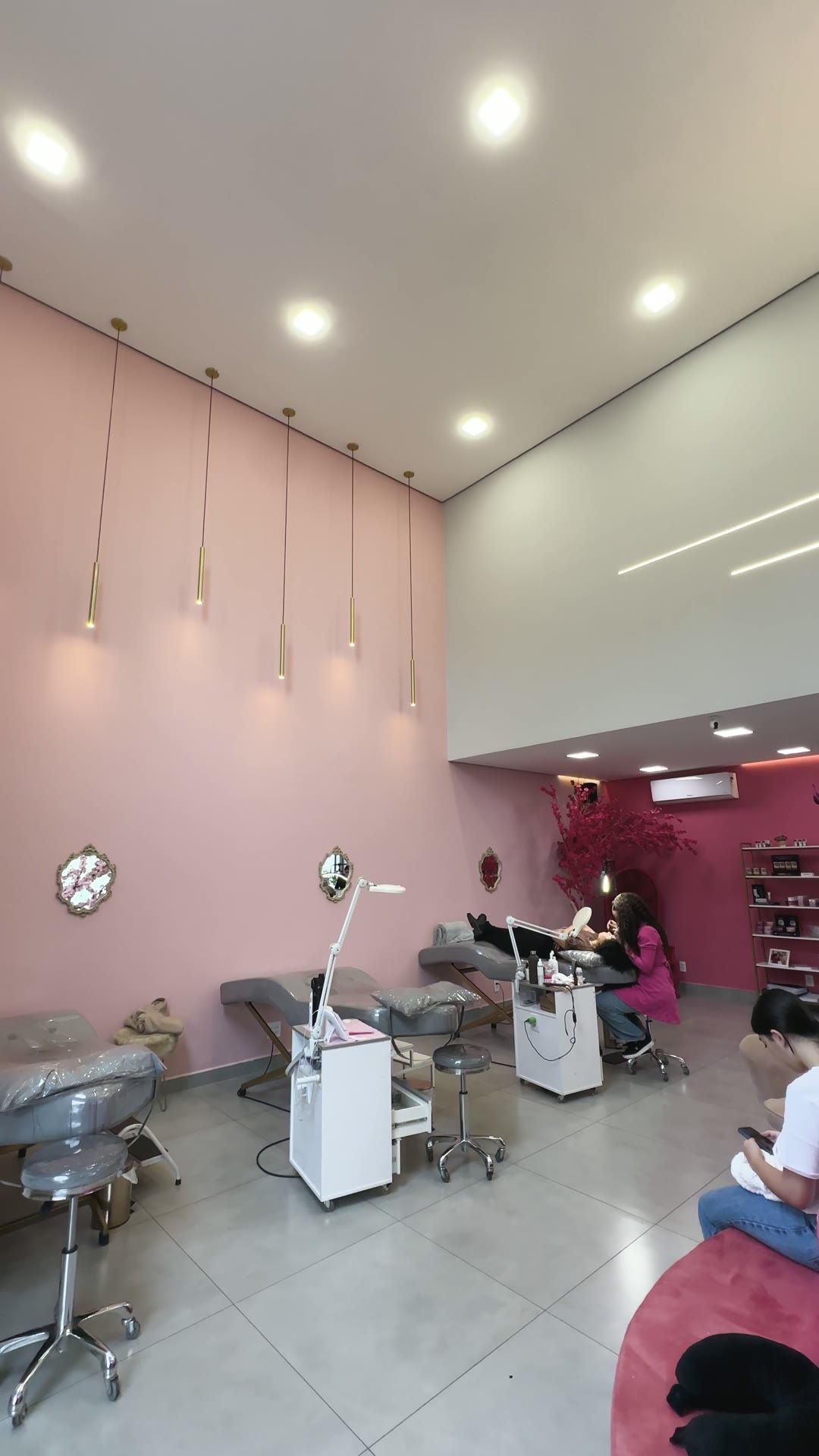 Salão de atendimento amplo, com pé-direito alto, macas e clientes sendo atendidas