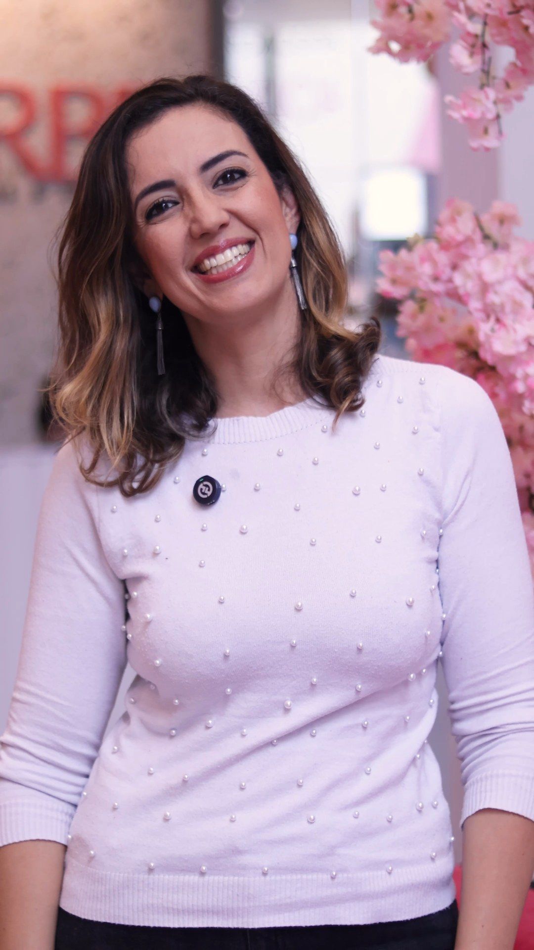 Dani Barbe em pé na Clínica da Barbe, com árvore de flores rosa ao fundo